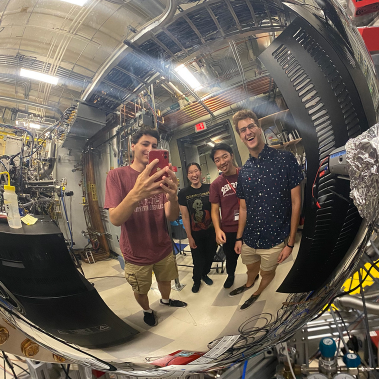4 smiling researchers reflected in stainless steel lab equipment
